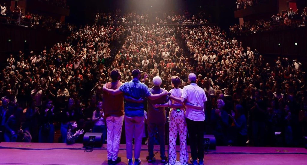 Gilberto Gil e sua equipe olhando para a plateia com luzes coloridas atrás