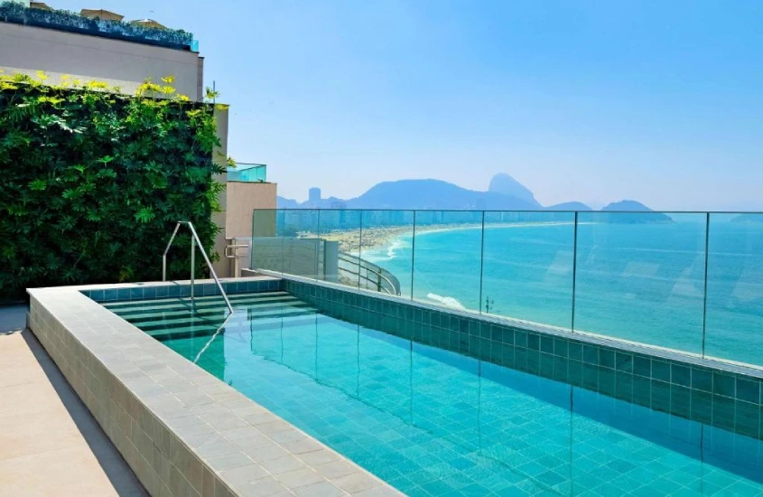 Em um dia de sol, área de piscina do Grand Mercure Rio de Janeiro Copacabana com vista da praia e parede de plantas