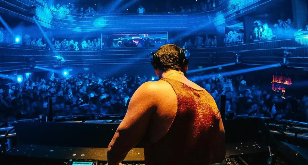 Dj tocando em balada com público na frente e luzes azuis