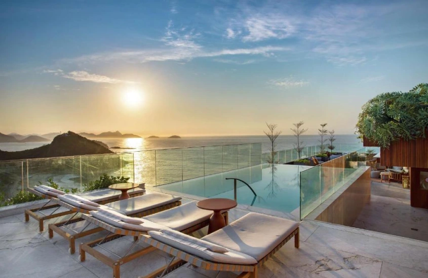 Durante o pôr do sol, área de piscina do Hilton Copacabana com espreguiçadeiras, plantas decorativas e vista da praia