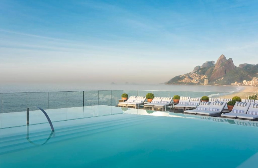 Em um dia ensolarado, cobertura do hotel Fasano com piscina de borda infinita, espreguiçadeiras e paisagem da praia e da ilha