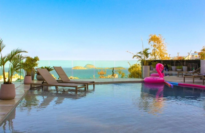 Em um dia de sol, área de piscina na cobertura do L'homme Hotel com flores decorativas, espreguiçadeiras, vóias e vista da praia e da ilha