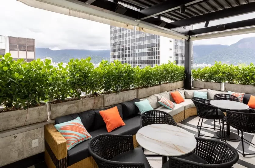 Em um dia de sol, cobertura do Mar Ipanema Hotel com plantas decorativas, sofás, mesas e almofadas coloridas