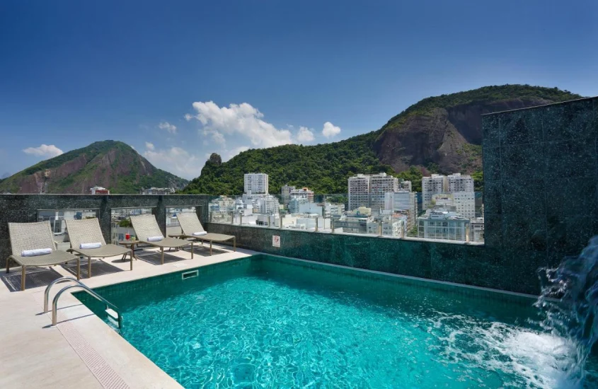 Em um dia de sol, cobertura do Hotel Mirasol com piscina, cascata, espreguiçadeiras, paisagem e montanhas ao redor