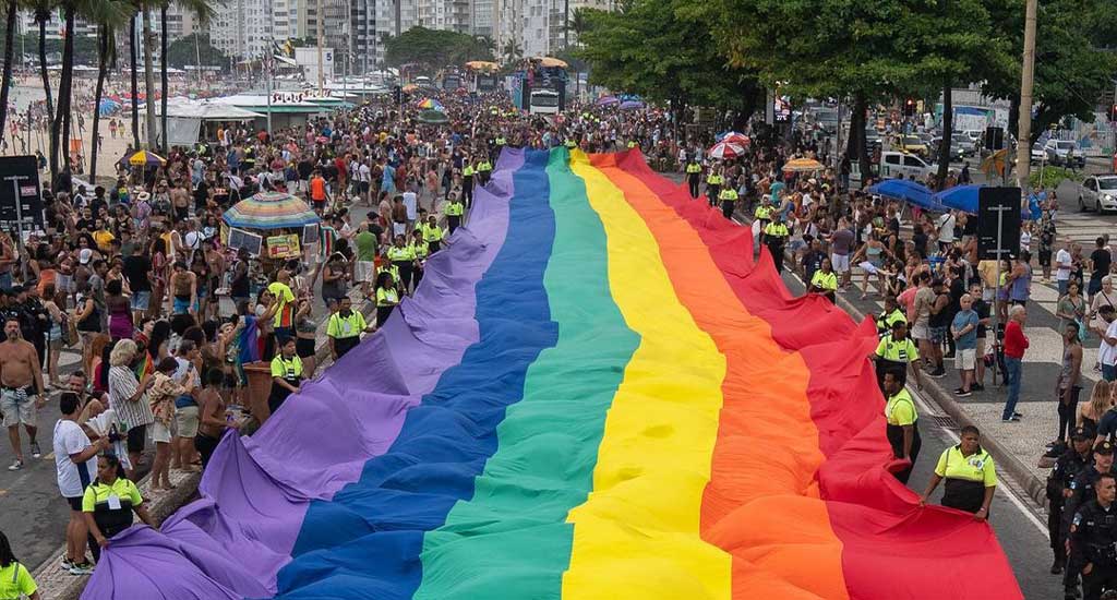 Vista aérea da parada gay com bandeirão lgbt, pessoas e árvores ao redor