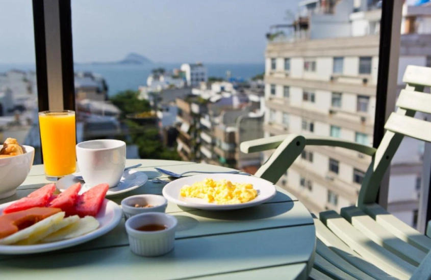 Em um dia de sol, mesa de café da manhã do Rtiz Leblon com paisagem dos prédios e da praia