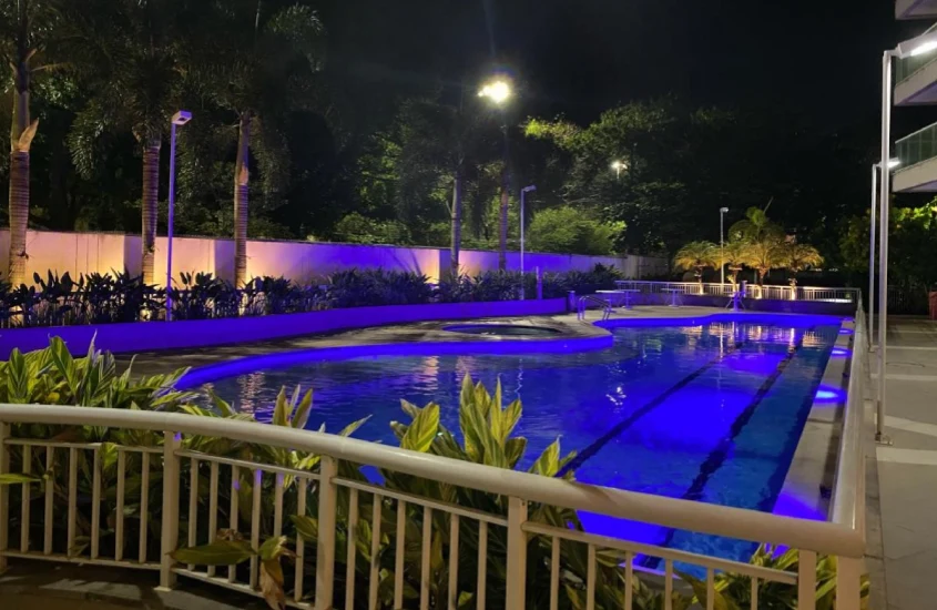 Durante a noite, área de lazer do Suite e Flat Premium com piscina e flores, plantas e árvores decorativas