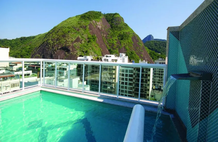 Em um dia de sol, piscina na cobertura do Hotel Bandeira com cascata e vista das montanhas