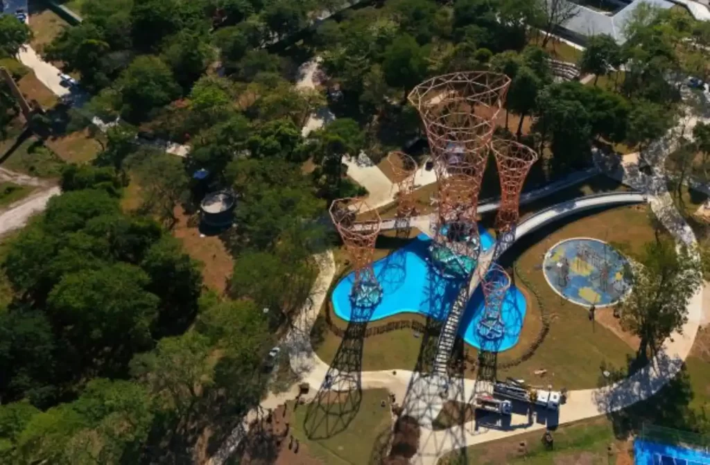 Em um dia de sol, vista aérea do Parque Realengo Susana Naspolini com piscinas, esculturas e árvores ao redor