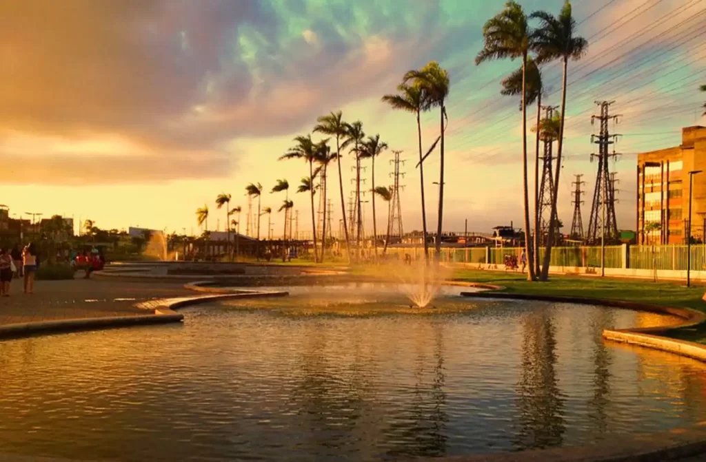 Durante o entardecer, Parque de Madureira com lagos com chafarizes, árvores e pessoas ao redor