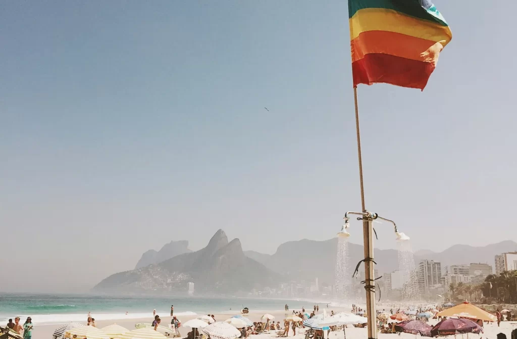 Em um dia de sol, paisagem do posto 9 com bandeira lgbt, pessoas ao redor e duchas