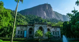 Em um dia ensolarado, fachada do Parque Lage com árvores ao redor e montanha atrás