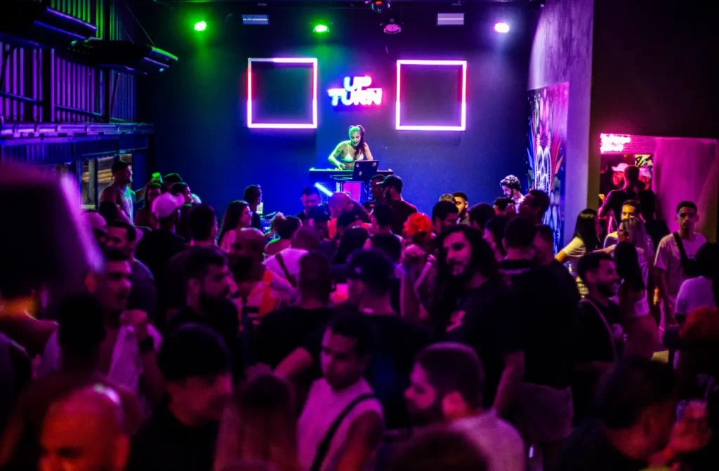 Balada com luzes coloridas, dj no palco e pessoas se divertindo