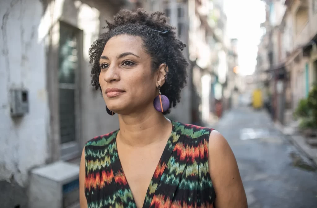 Em um dia de sol, Marielle Franco andando pelas ruas de uma periferia