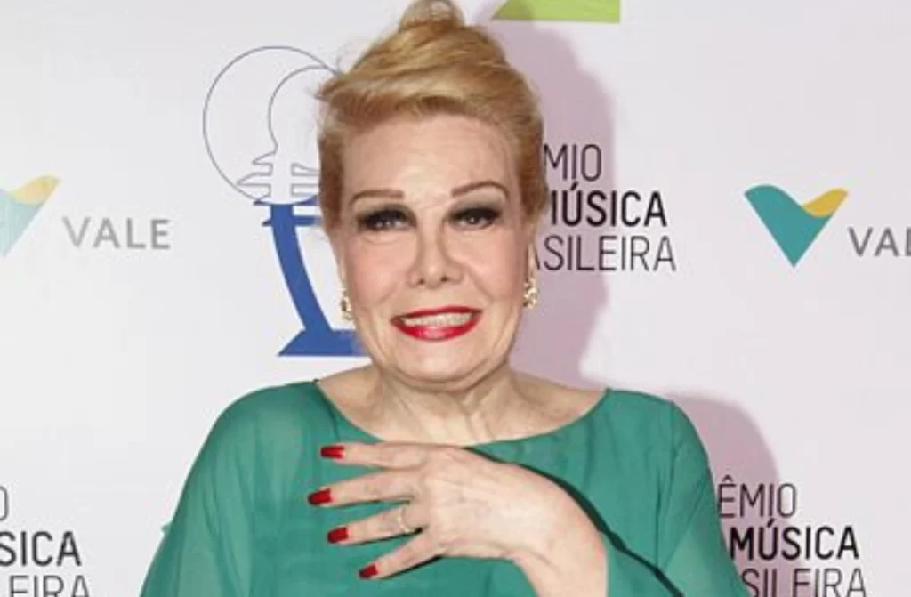 Artista Rogéria sendo fotografada em evento com roupa verde e unhas vermelhas