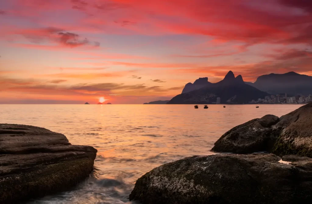 Durante o por do sol, paisagem da praia com montanhas ao redor e céu colorido refletido no mar