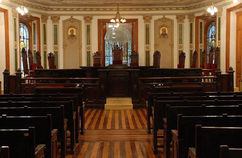 Interior do Centro Cultural Justiça Federal com bancos de madeira, luzes amarelas e mesa de jantar