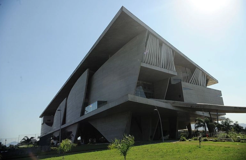 Em um dia de sol, fachada da cidade das artes com gramado e árvores ao redor