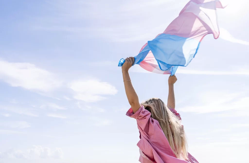 Em um dia de sol, mulher loira segurando bandeira trans