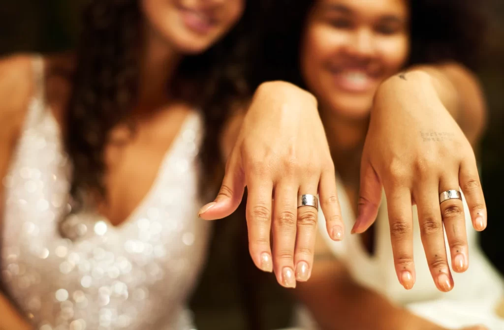 Duas mulheres vestidas de noivas mostrando as alianças de casamento