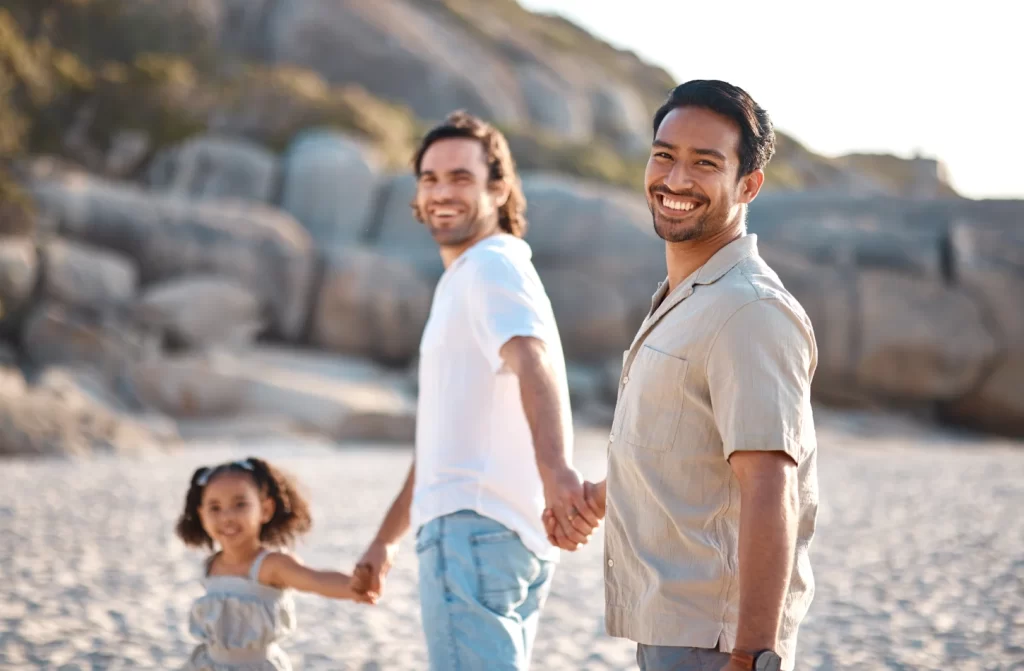 Casal homossexual de mãos dadas com criança em praia com pedras ao redor