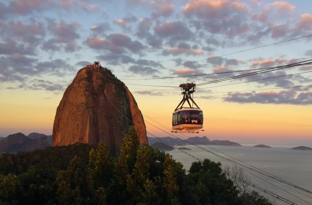 Em um final de tarde, bondinho subindo para o Pão de Açúcar com paisagem da cidade no fundo