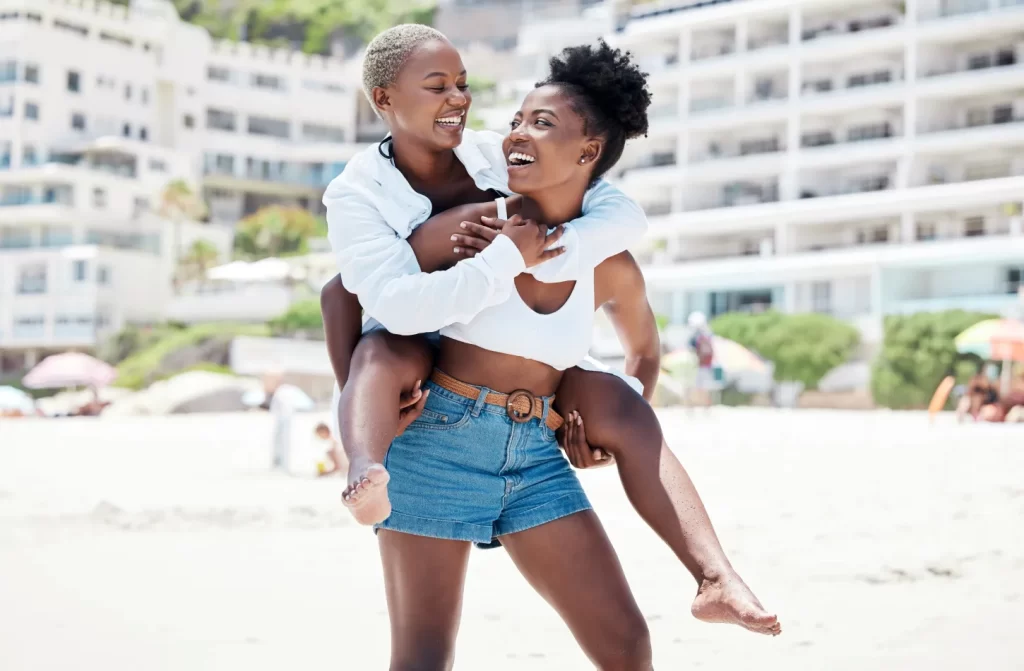 Em um dia de sol, casal de lésbicas com praia na frente e hotel atrás.