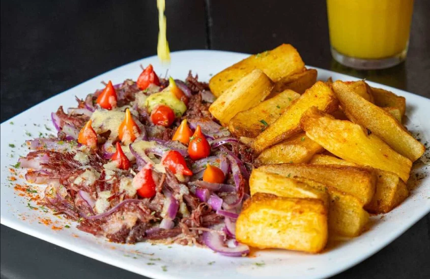 Prato do Mãe Joana com carne de seca, mandioca, pimentas biquinho e suco do lado