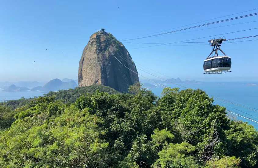 Em um dia de sol, paisagem do Pão de açucar com bondinho e árvores ao redor