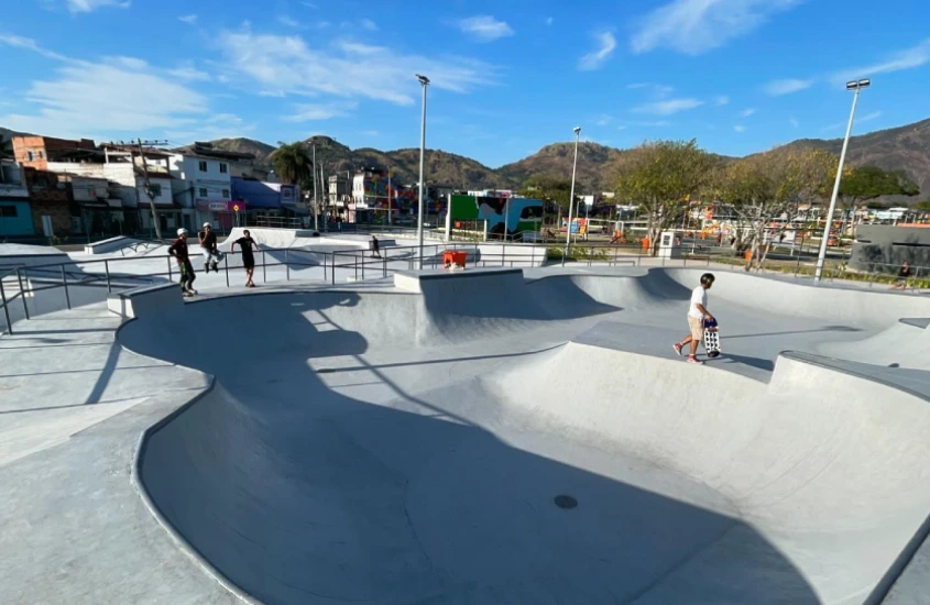 Em um dia de sol, pista de skate do Parque Realengo Susana Naspolini com pessoas se divertindo e árvores ao redor