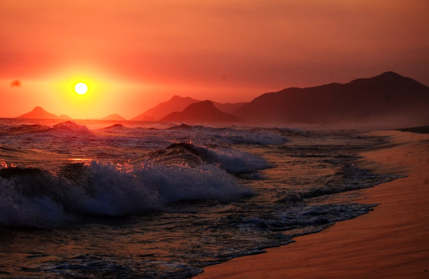 Durante o pôr do sol, Praia da Reserva com as ondas quebrando e sol refletido no mar