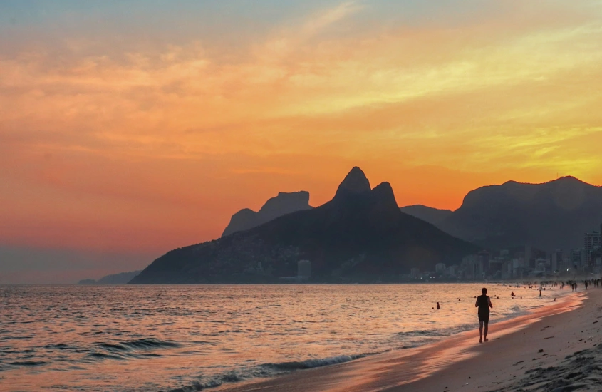 Durante o entardecer, Praia de Ipanema com pessoas se banhando e montanhas atrás