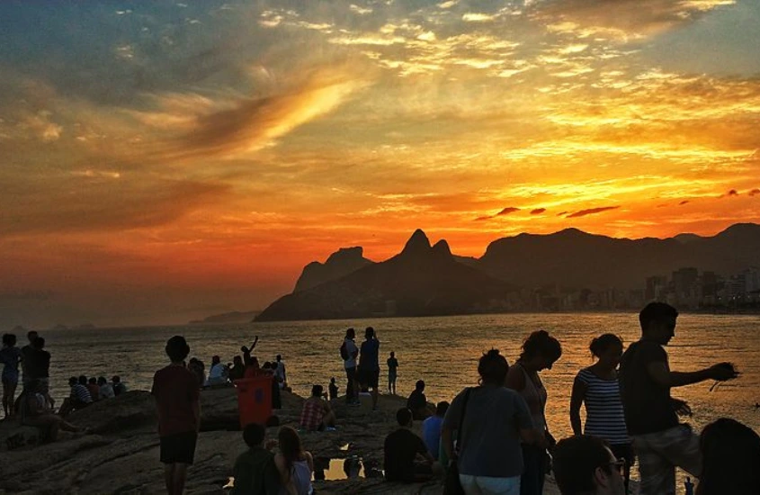 Pôr do shoe na Praia do Arpoador com pessoas assistindo, mar refletindo o céu e ilha no fundo