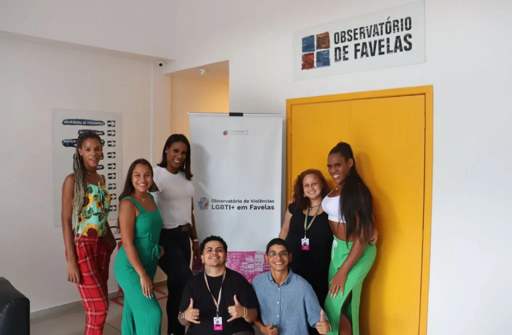 Pessoas de um projeto LGBT com banner no meio e pintura escrito "observatório de favela"