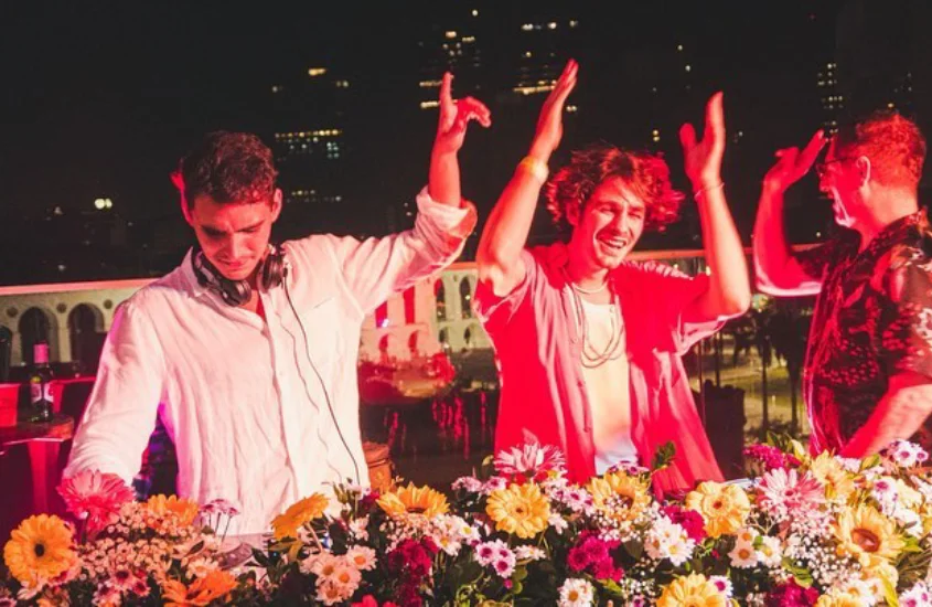 Djs iluminados por luzes vermelhas no Selina Rooftop com flores na mesa dos astistas