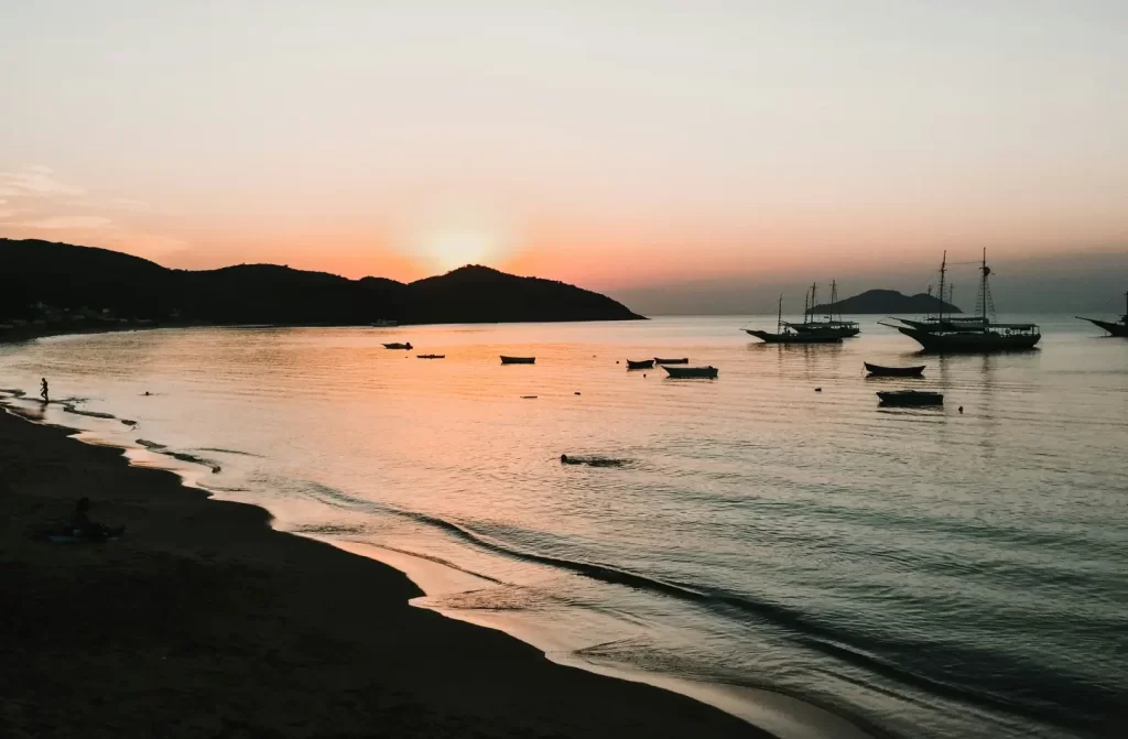 Durante o pôr do sol, praia com barcos no mar e água refletindo o sol