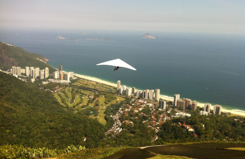 Em um dia ensolarado, vista da altura Pedra Bonita com pessoa fazendo parapente, cidade e praia embaixo