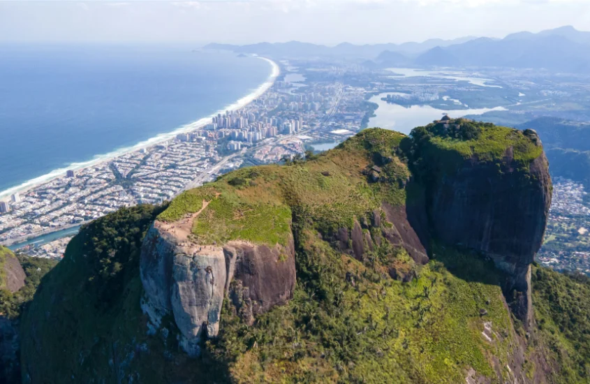 Em um dia de sol, paisagem da Pedra da Gávea com cidade e praia no fundo