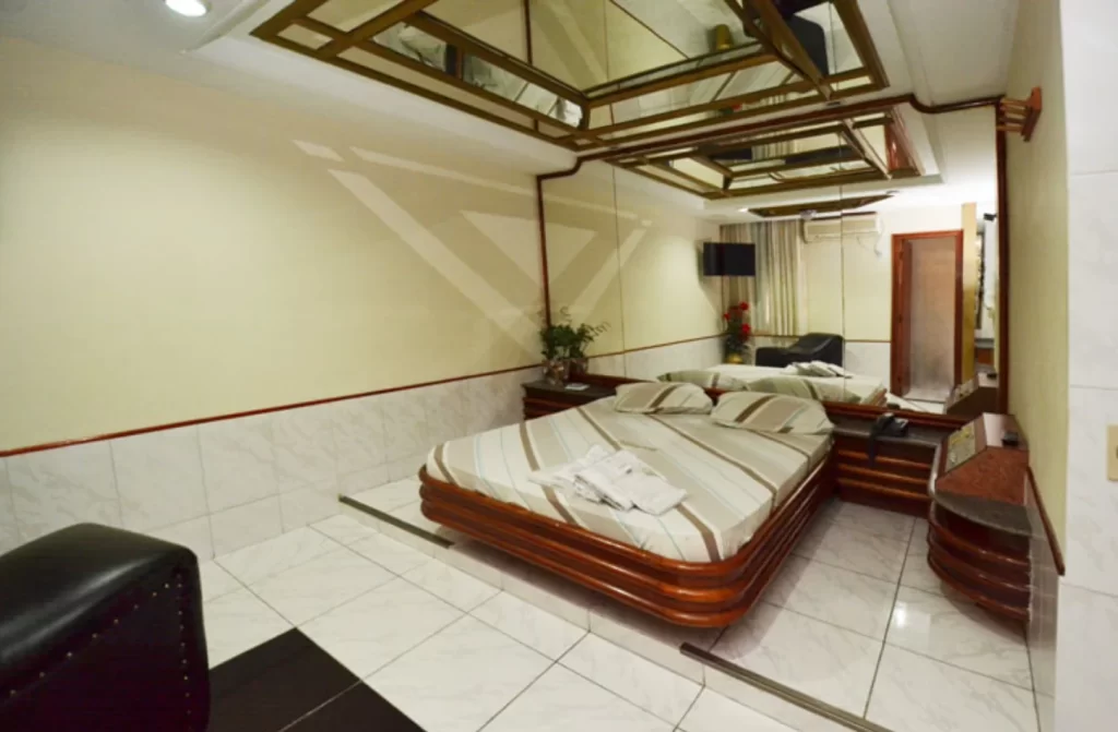 Quarto do Hotel Bariloche com cama de casal, móveis pretos e de madeira com espelhos ao redor