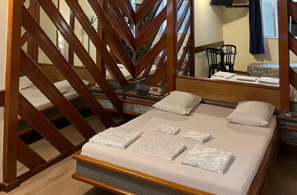 Quarto do Hotel Paraguai com cama de casal, estruturas de madeira e espelhos ao redor