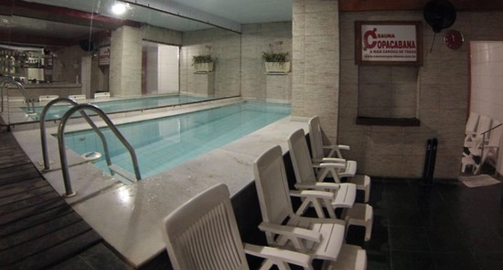 Interior da sauna com cadeiras e piscina do lado