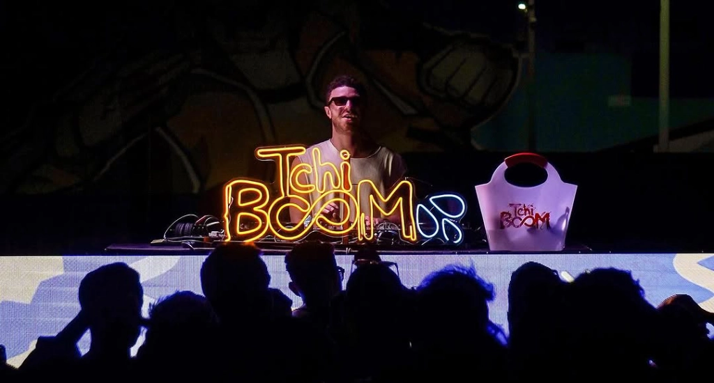 Dj tocando com letreiro iluminado com a logo doa festa