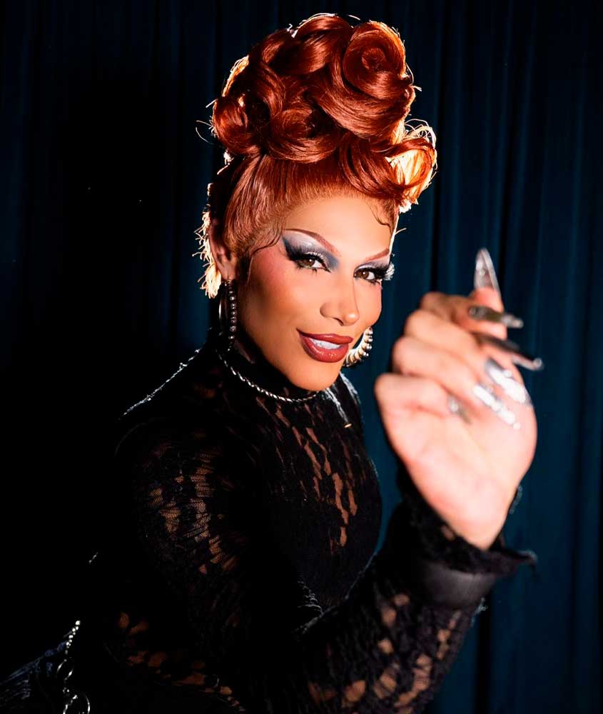 Drag segurando caneta e sorrindo